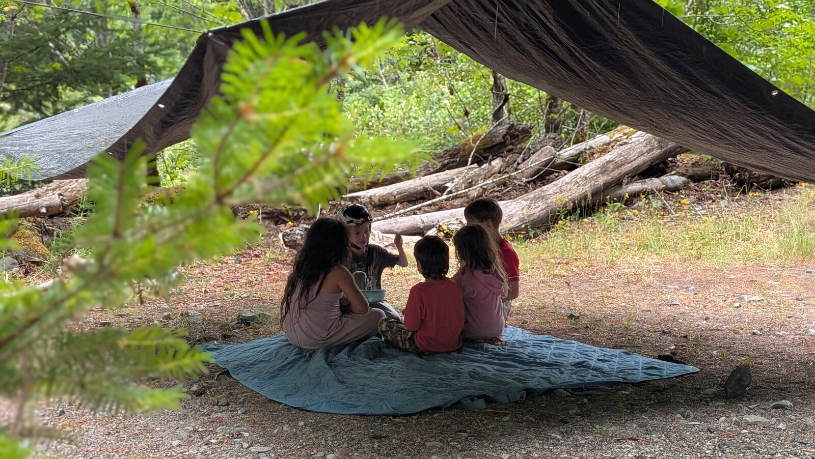 Children sitting together under a tarp shelter